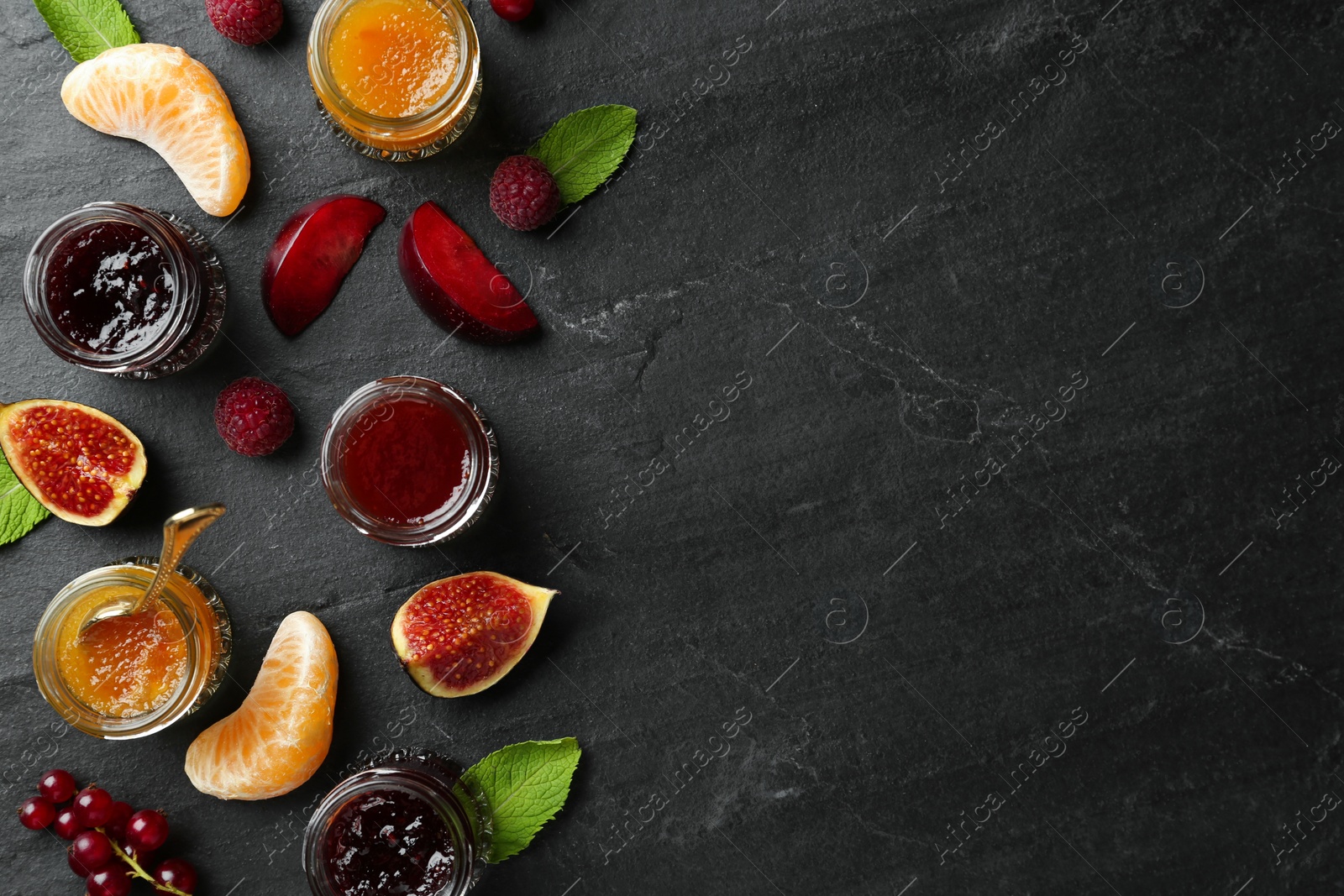 Photo of Jars of different jams and fresh ingredients on black table, flat lay. Space for text