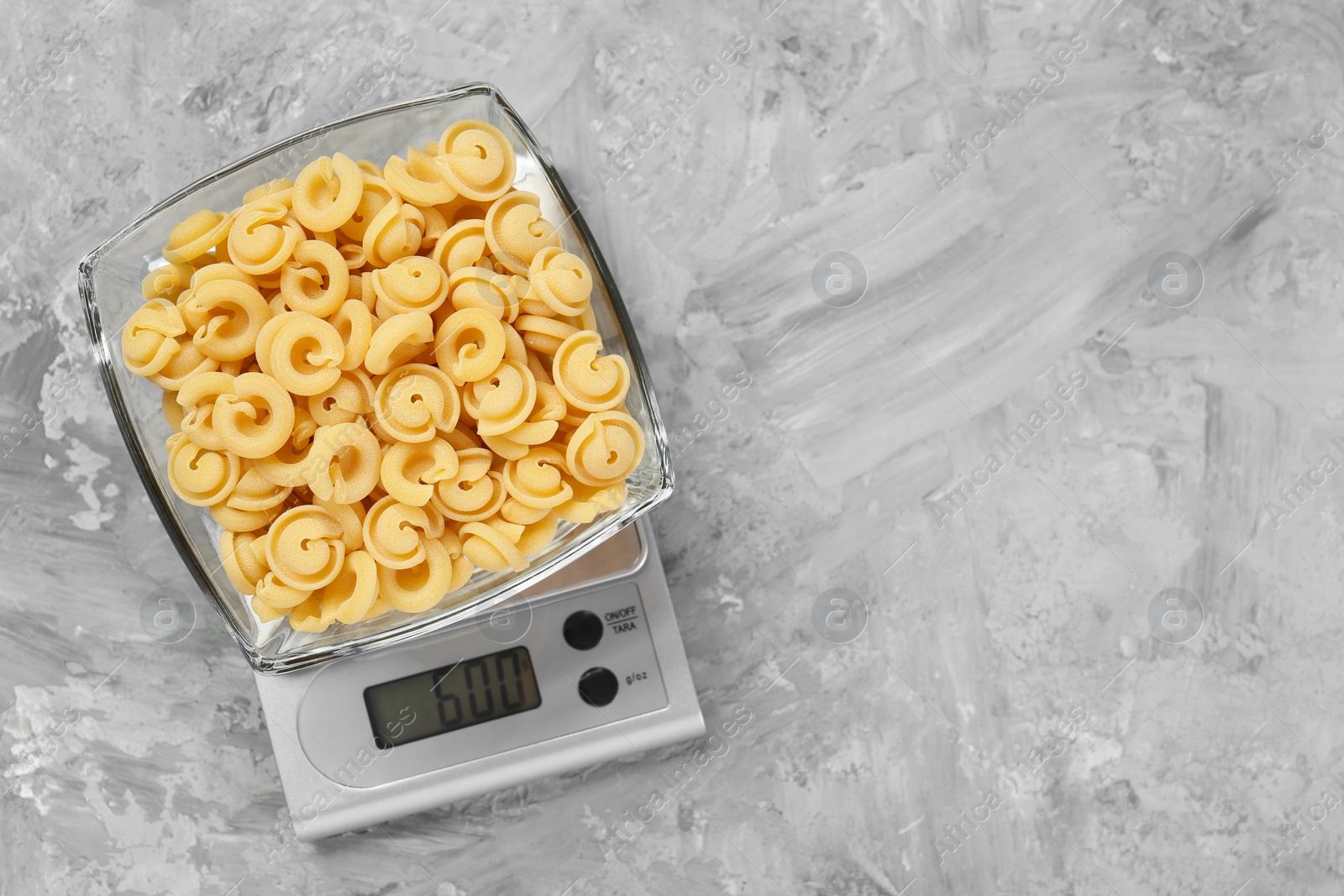 Photo of Kitchen scale with bowl of pasta on grey textured table, top view. Space for text