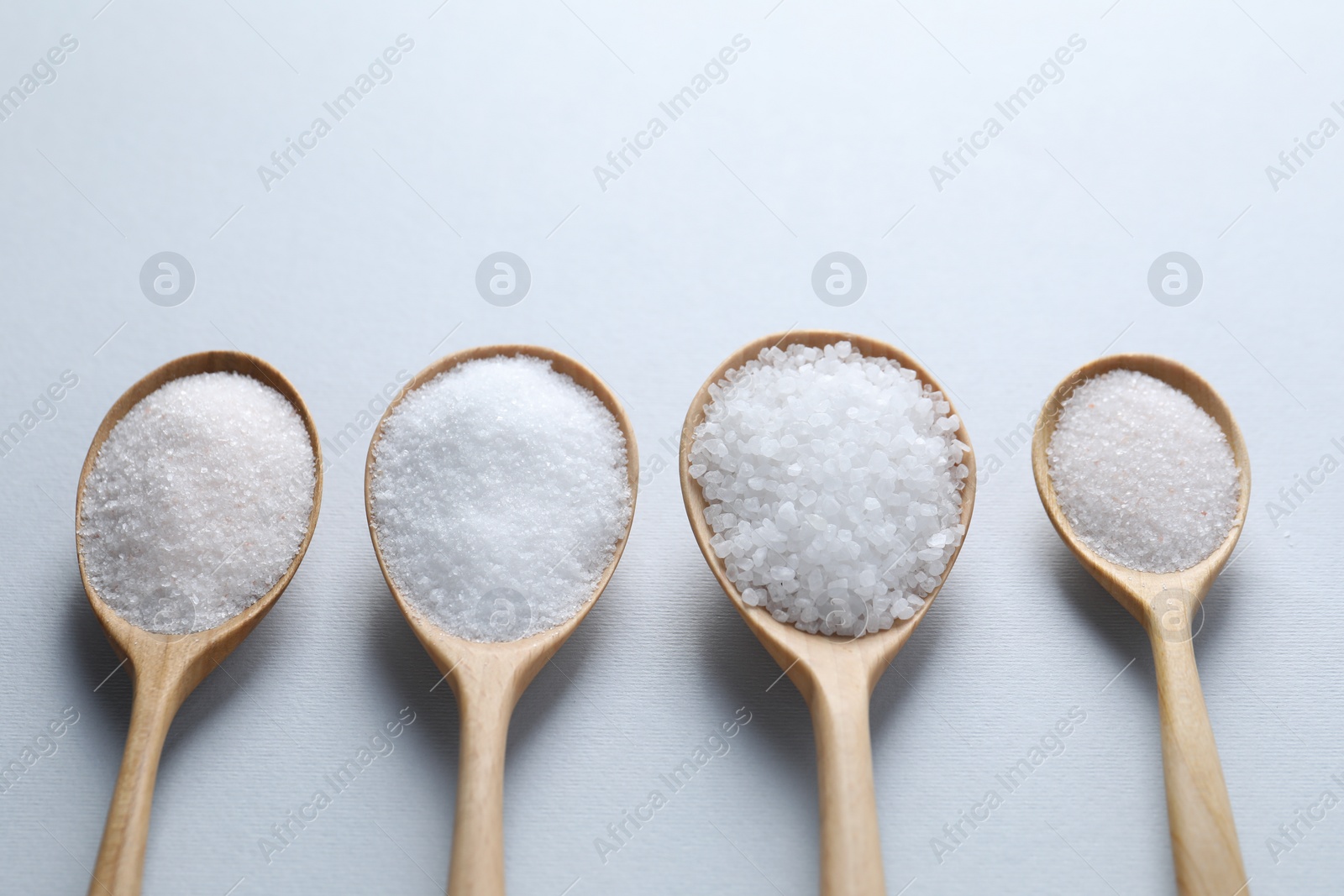 Photo of Organic white salt in spoons on light grey background, closeup. Space for text