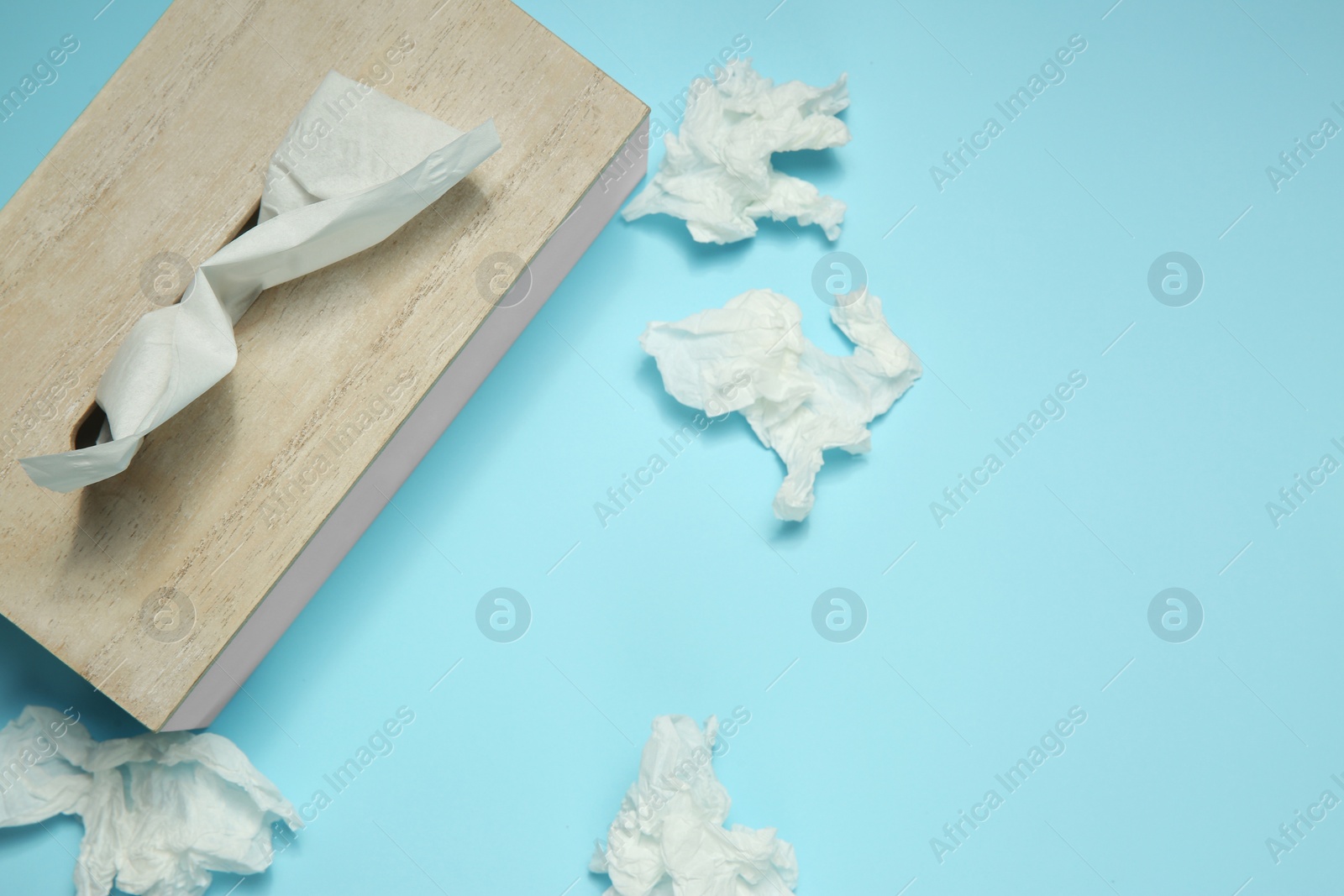 Photo of Used paper tissues and wooden holder on light blue background, flat lay. Space for text