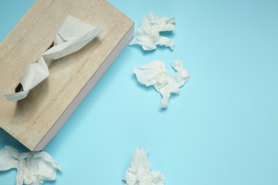 Photo of Used paper tissues and wooden holder on light blue background, flat lay. Space for text