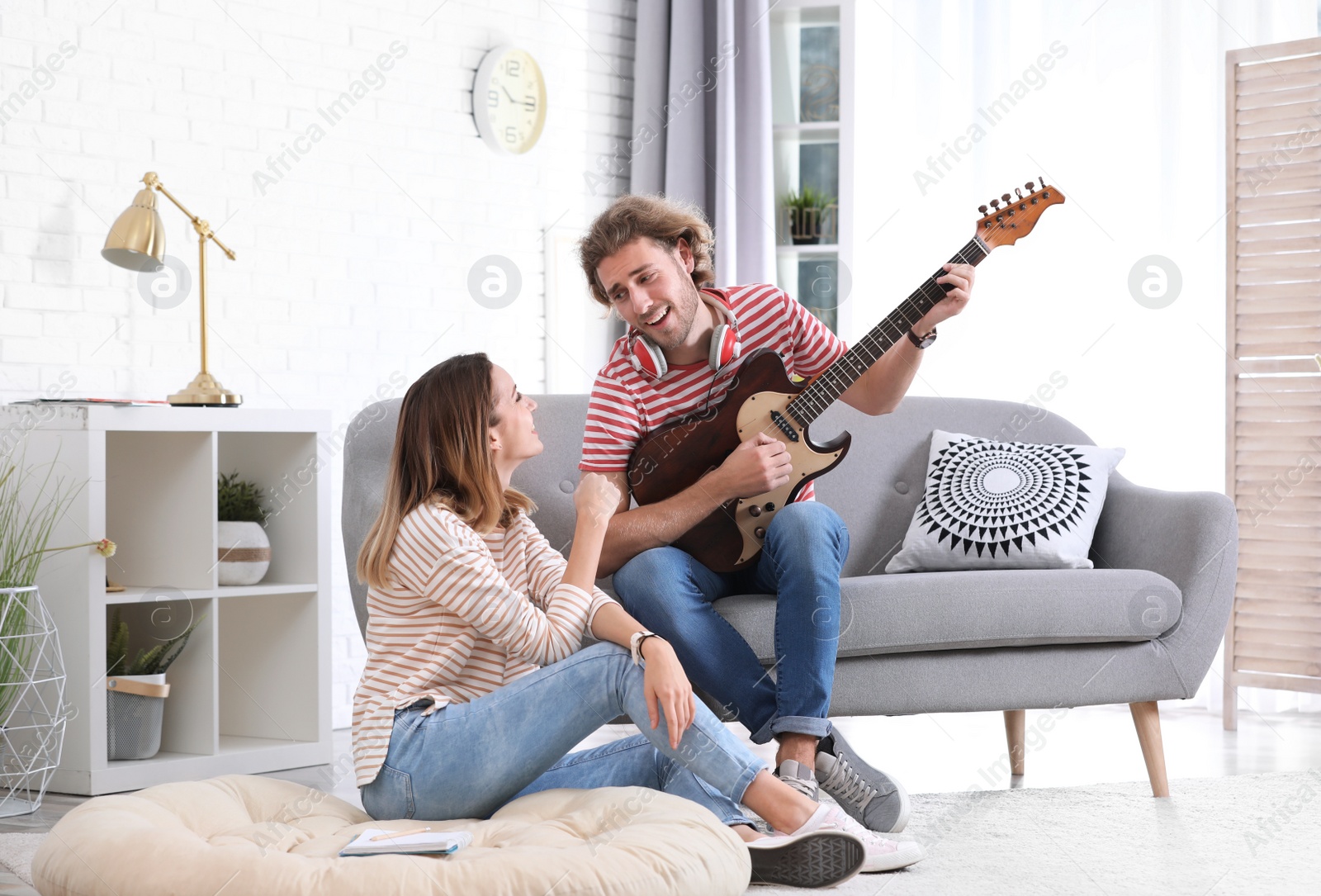 Photo of Young man playing electric guitar for his girlfriend in living room