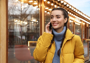 Photo of Young woman talking on mobile phone near cafe decorated for Christmas