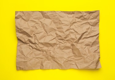 Sheet of crumpled brown paper on yellow background, top view