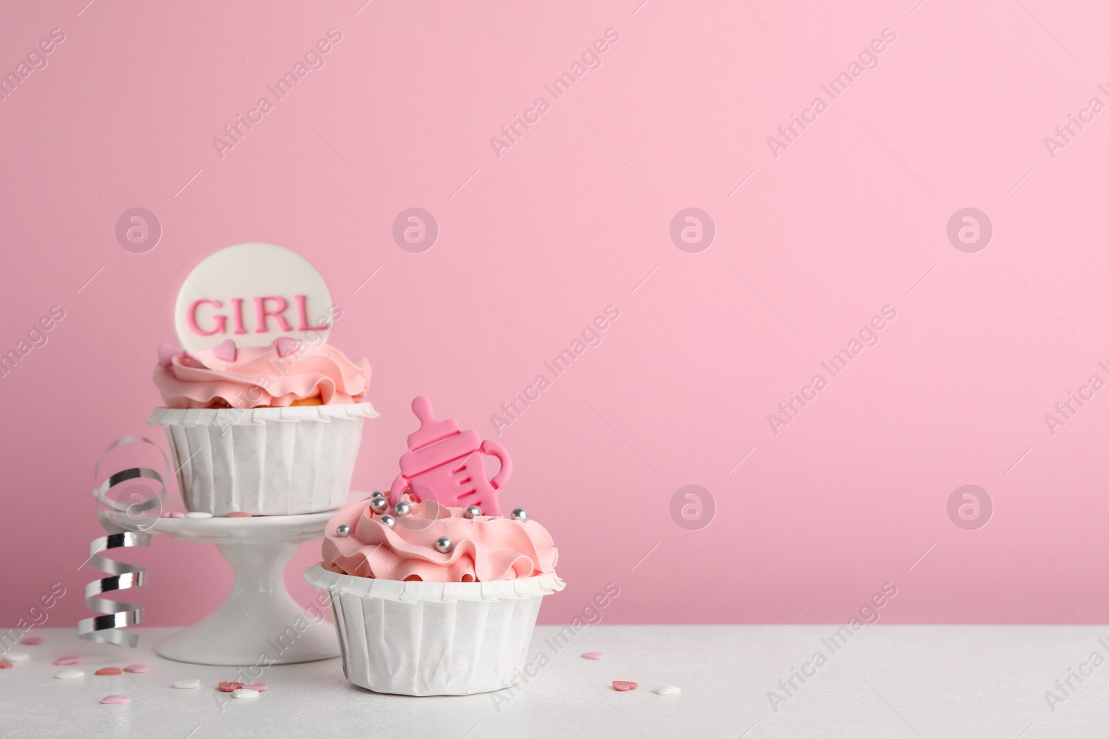 Photo of Baby shower cupcakes with toppers on white table against pink background, space for text