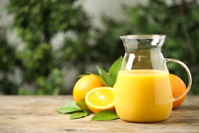 Photo of Jug of orange juice and fresh fruits on wooden table. Space for text