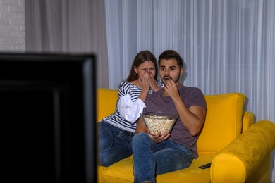 Photo of Couple with popcorn watching TV together on sofa in living room