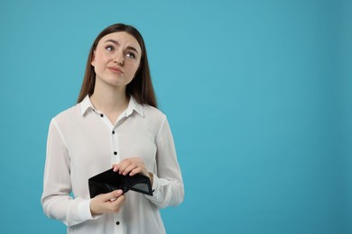 Sad woman showing empty wallet on light blue background, space for text