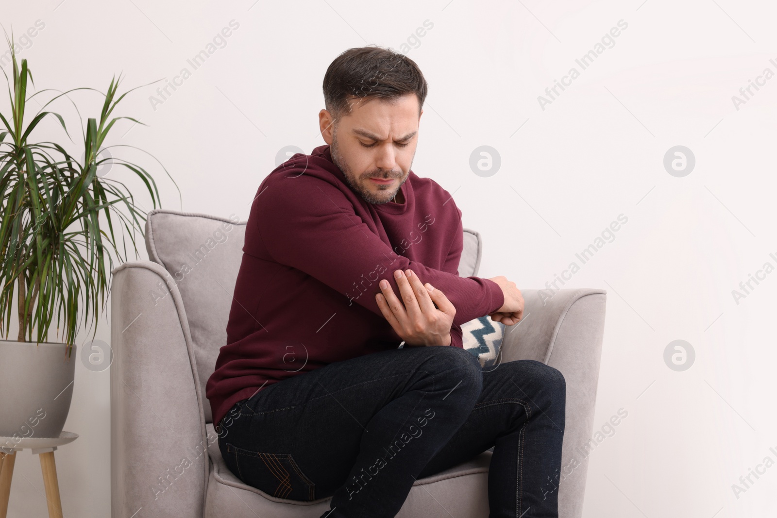 Photo of Man suffering from pain in his elbow on armchair indoors