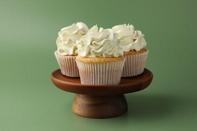 Tasty vanilla cupcakes with cream on green background