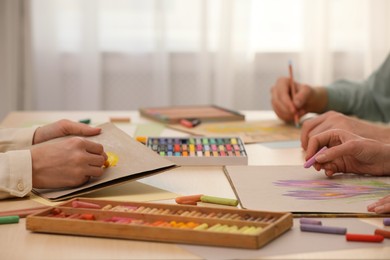 Photo of Artists drawing with soft pastels and pencils at table indoors, closeup