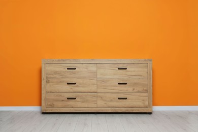 Photo of New wooden chest of drawers near orange wall indoors