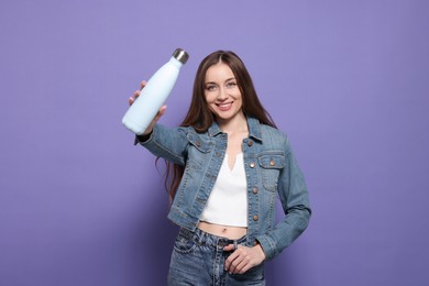 Beautiful young woman with thermos bottle on purple background