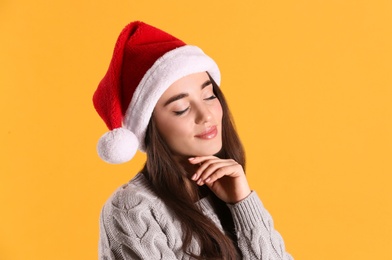 Beautiful woman wearing Santa Claus hat on yellow background