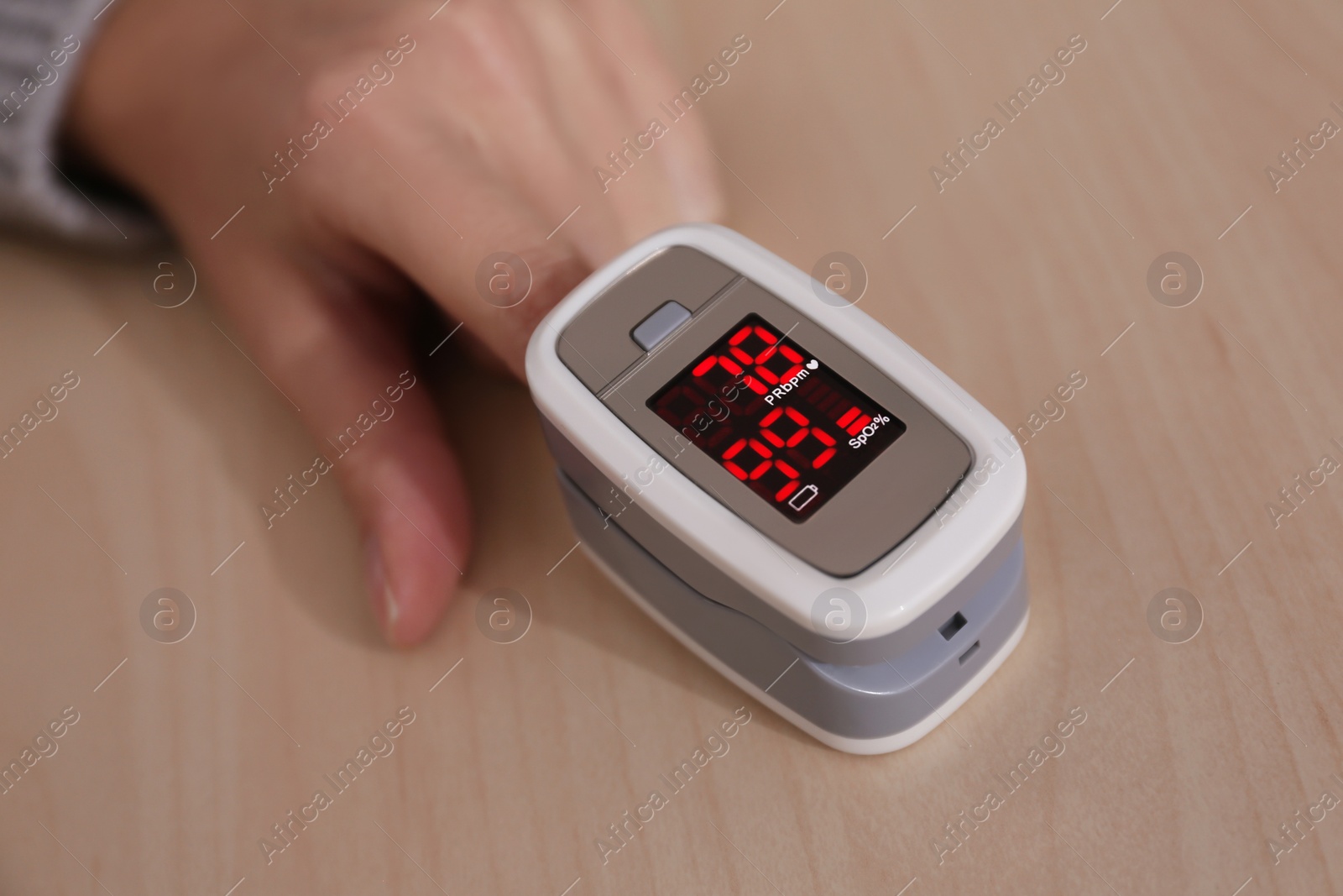 Photo of Woman measuring oxygen level with modern fingertip pulse oximeter at wooden table, closeup