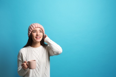 Photo of Young woman in sweater with cup of hot coffee on color background, space for text. Winter season