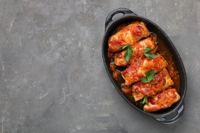 Delicious stuffed cabbage rolls cooked with tomato sauce on grey table, top view. Space for text