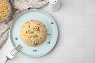 Delicious bulgur with vegetables and microgreens served on white tiled table, flat lay. Space for text