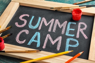 Text "SUMMER CAMP" on chalkboard, brushes and paints, closeup