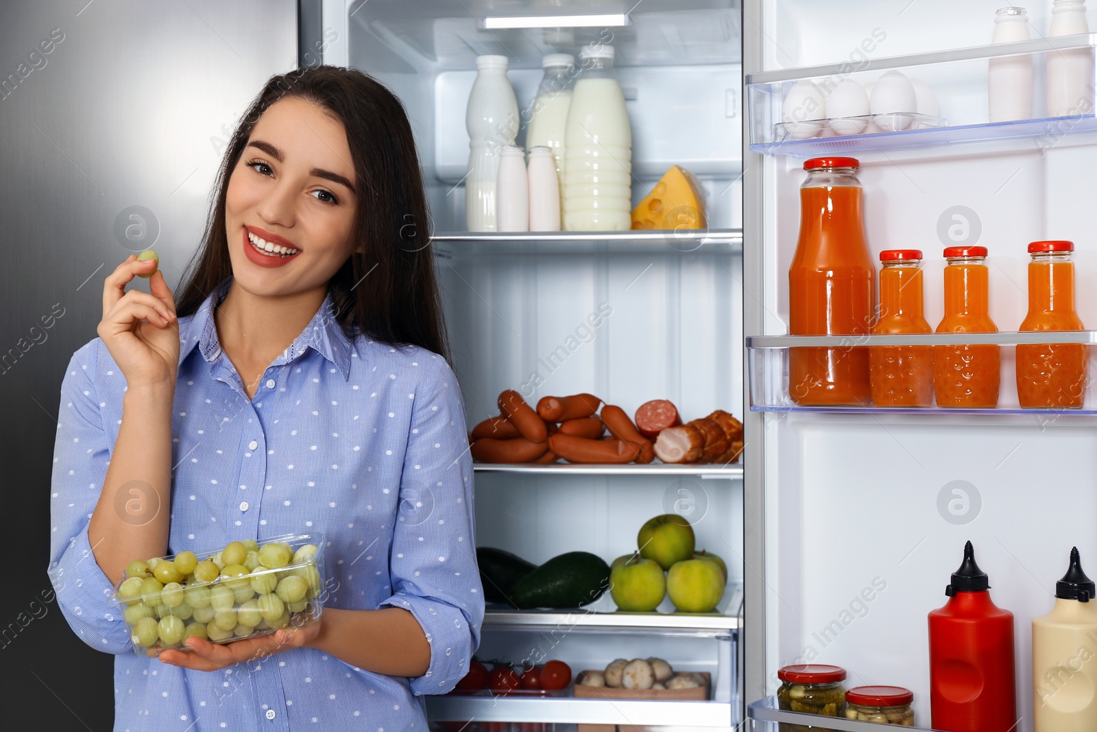 Photo of Happy young woman with grape near open refrigerator