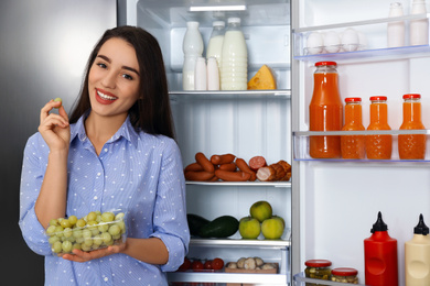 Happy young woman with grape near open refrigerator