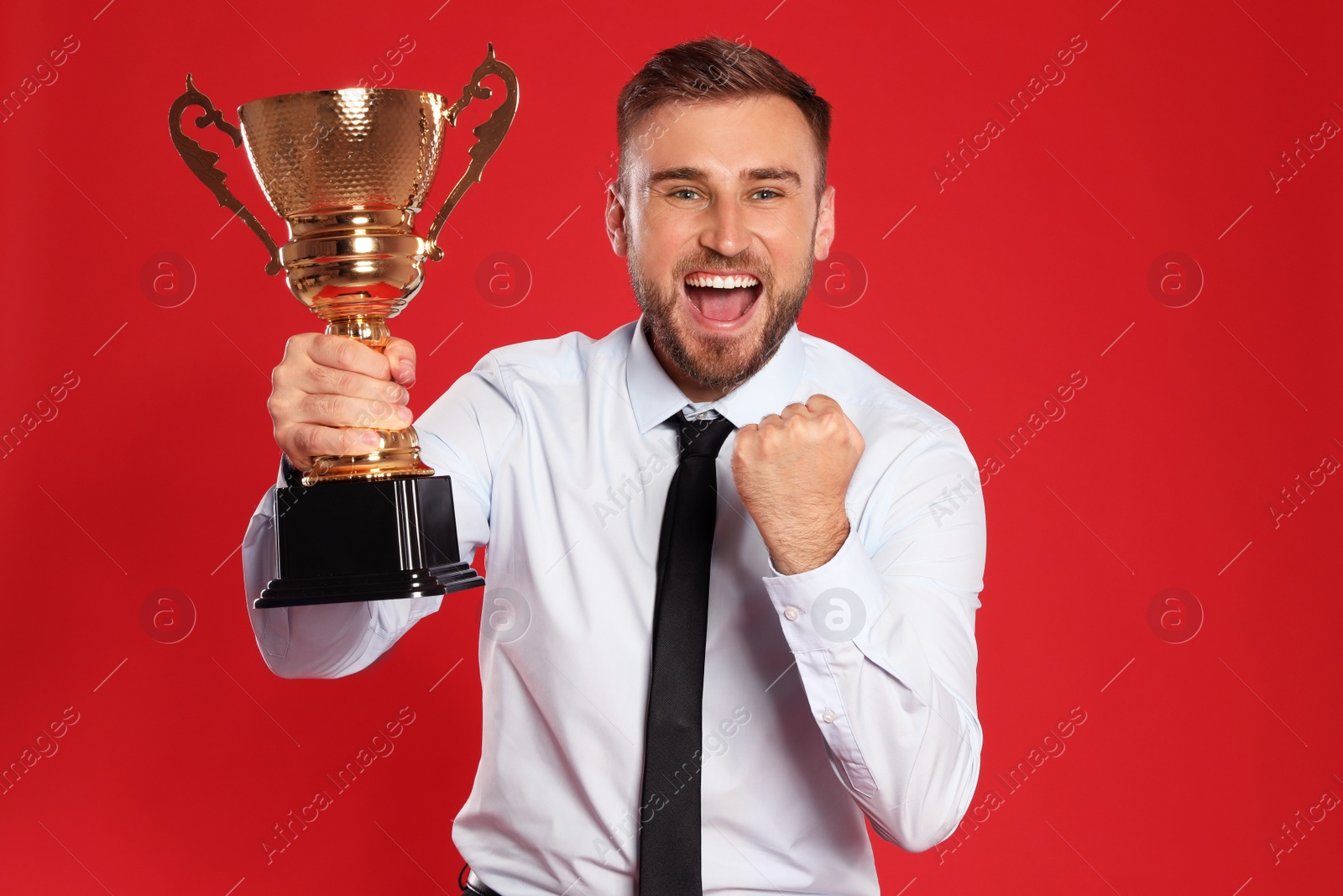 Photo of Portrait of happy young businessman with gold trophy cup on red background