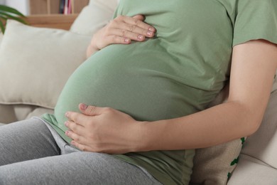 Photo of Pregnant woman touching belly in living room, closeup