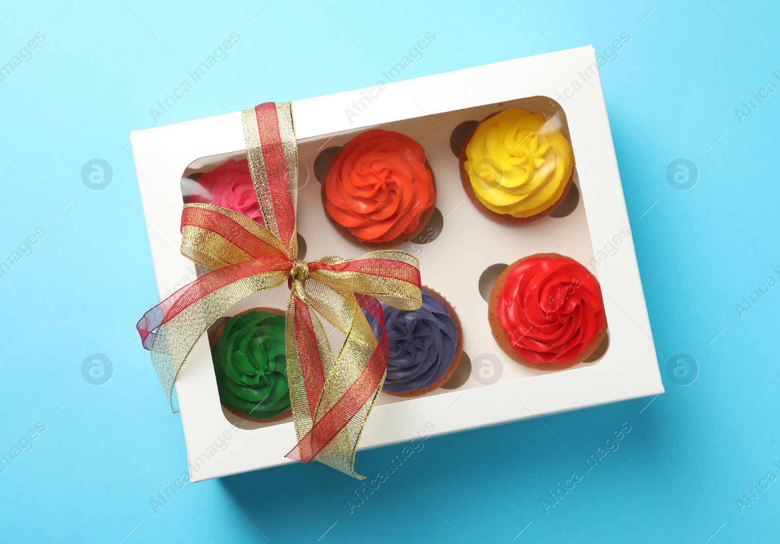 Photo of Box with delicious colorful cupcakes on light blue background, top view