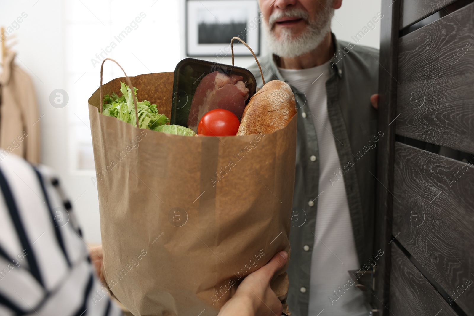 Photo of Courier giving paper bag with food products to senior man indoors, closeup