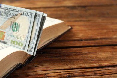 Photo of Open Bible with money on wooden table, closeup. Space for text