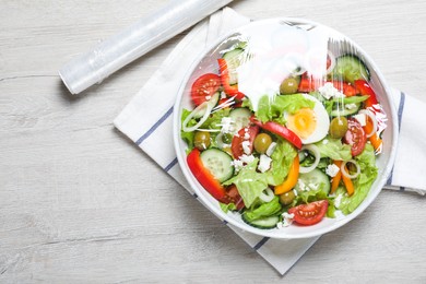 Photo of Bowl of fresh salad with plastic food wrap on white wooden table, flat lay