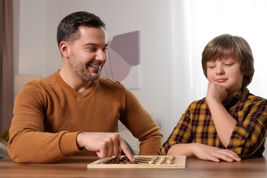 Photo of Father playing checkers with his son at table in room