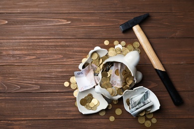Broken piggy bank with money and hammer on wooden background, top view. Space for text