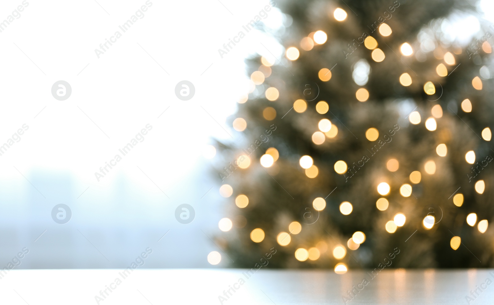 Photo of Blurred view of beautiful Christmas tree with yellow lights near window indoors, focus on table. Space for text