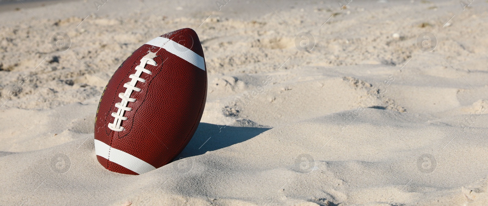 Photo of American football ball on beach. Space for text