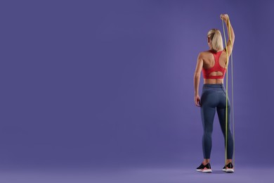 Athletic woman exercising with elastic resistance band on purple background, back view. Space for text