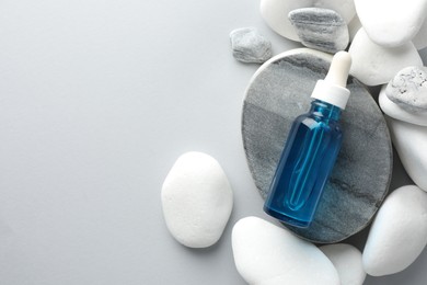 Bottle of face serum and stones on light grey background, top view. Space for text