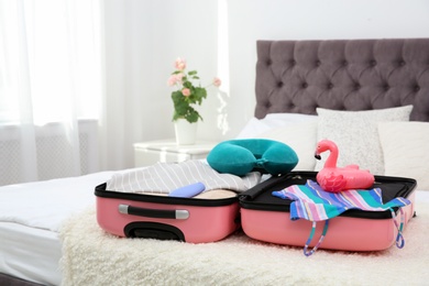 Photo of Modern suitcase with clothes packed for journey on bed indoors