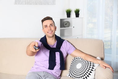 Photo of Handsome young man watching TV on sofa at home