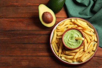 Photo of Plate with french fries, guacamole dip and avocado served on wooden table, flat lay. Space for text