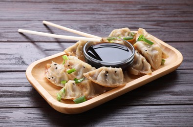 Photo of Delicious gyoza (asian dumplings) with green onions, soy sauce and chopsticks on wooden table