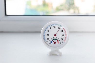 Photo of Round hygrometer with thermometer on window sill indoors