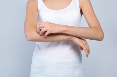 Young woman scratching arm on light background, closeup. Annoying itch