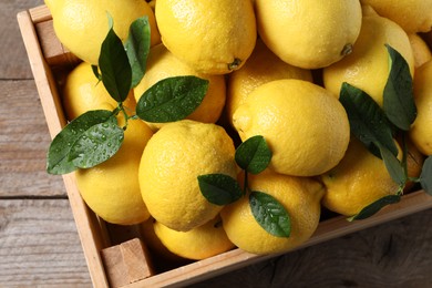 Fresh lemons and green leaves in crate on wooden table, top view