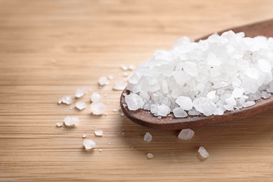 Photo of Spoon of white sea salt on wooden table, closeup with space for text. Spa treatment