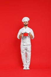 Photo of Professional chef with cooking pot on red background