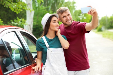 Beautiful young couple taking selfie near car