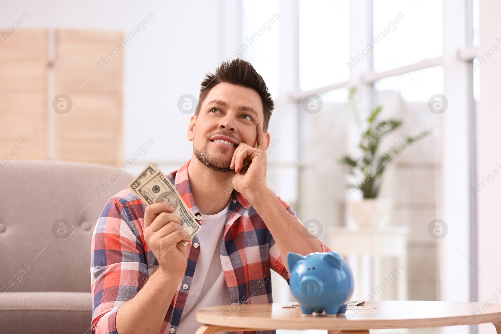 Photo of Man with piggy bank and money at home