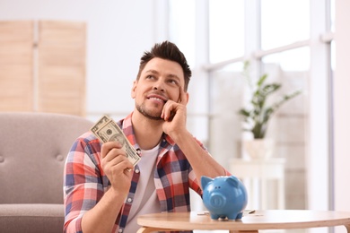 Man with piggy bank and money at home