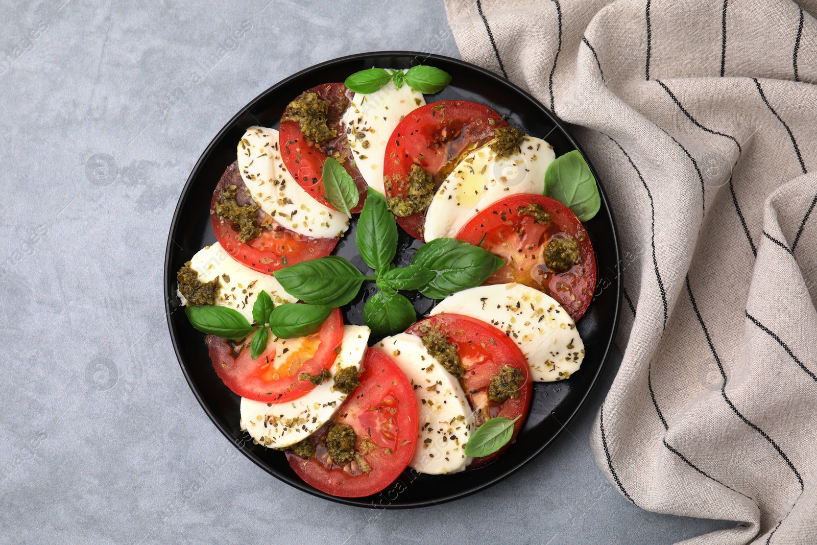 Photo of Plate of delicious Caprese salad with pesto sauce on grey table, top view